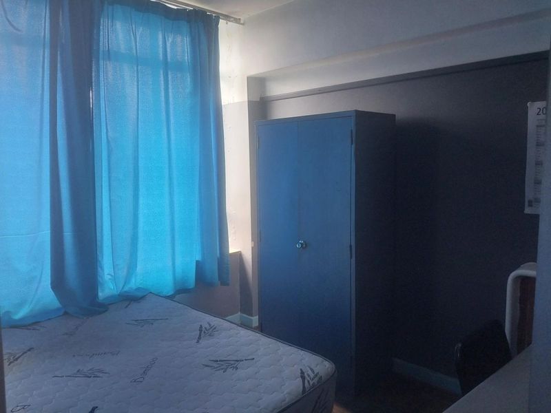 A bedroom featuring a window with curtains and painted walls showing signs of wear.