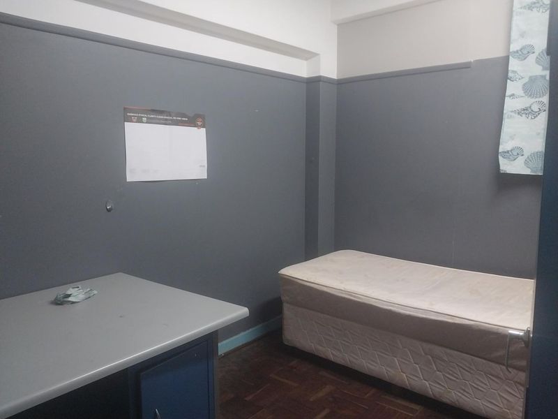 A compact bedroom featuring dark grey walls, parquet flooring, and a built-in desk area, offering a functional space ready for modernization.