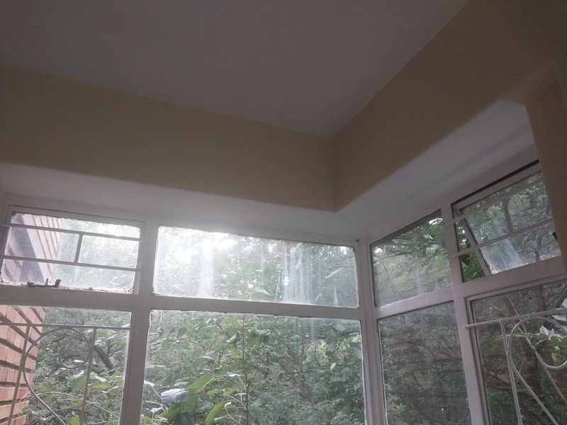 Enclosed balcony area featuring aluminium window frames with security bars, offering a view of the surrounding greenery.