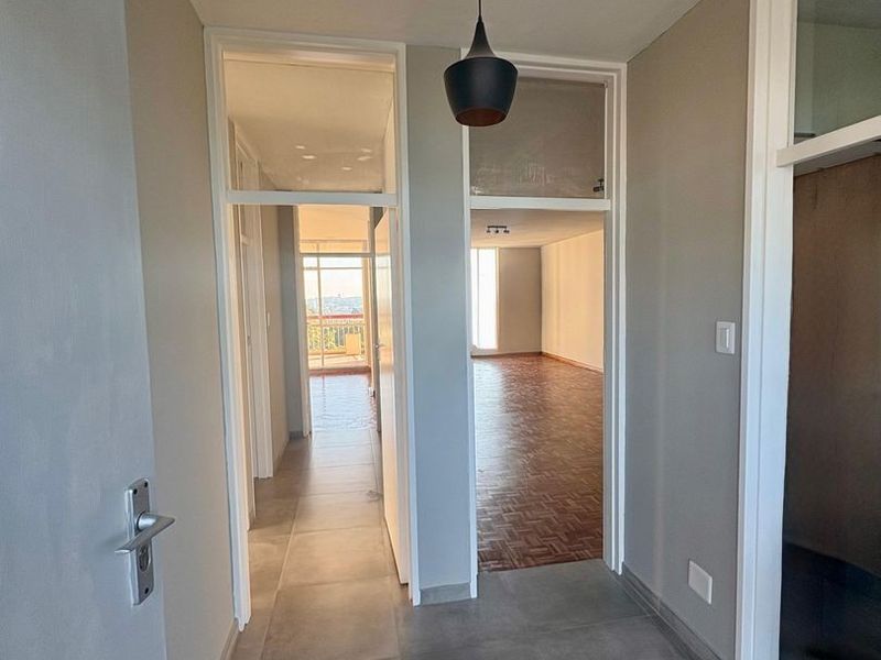 A bright, empty hallway featuring modern grey floor tiles, parquet flooring in the adjacent rooms, and transom windows above the internal doorways.