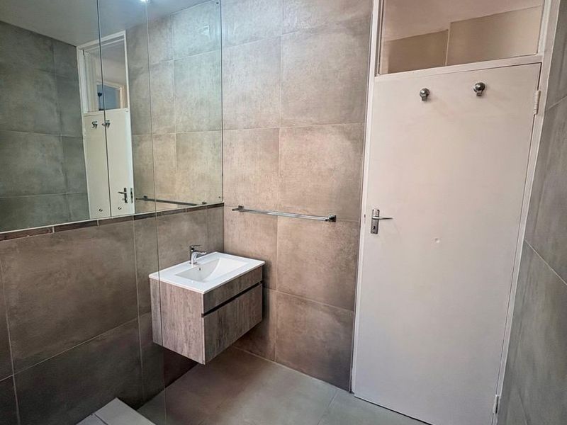 Modern bathroom featuring a wall-mounted vanity with integrated basin, large mirror, glass shower screen, and neutral floor-to-ceiling tiling.