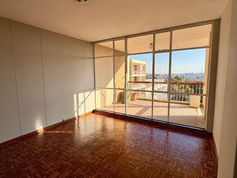 Bright and spacious living area featuring classic parquet flooring and large glass doors leading out to a private balcony with city views.
