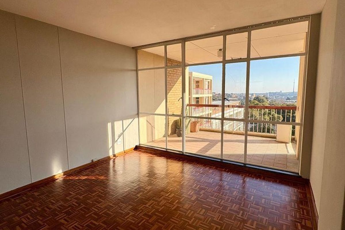 Bright and spacious living area featuring classic parquet flooring and large glass doors leading out to a private balcony with city views.