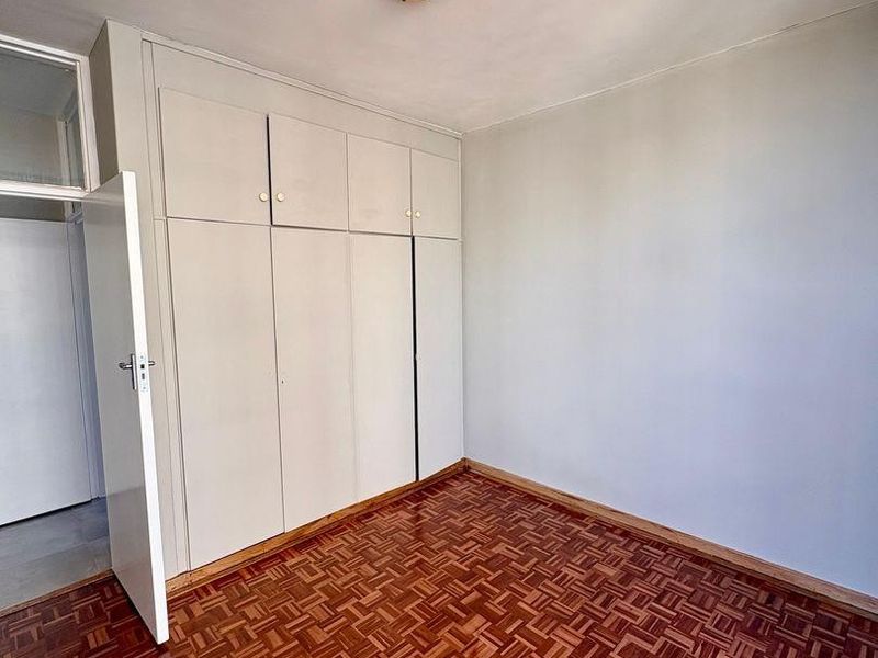A bright, empty bedroom featuring classic parquet flooring and ample built-in cupboard storage space.