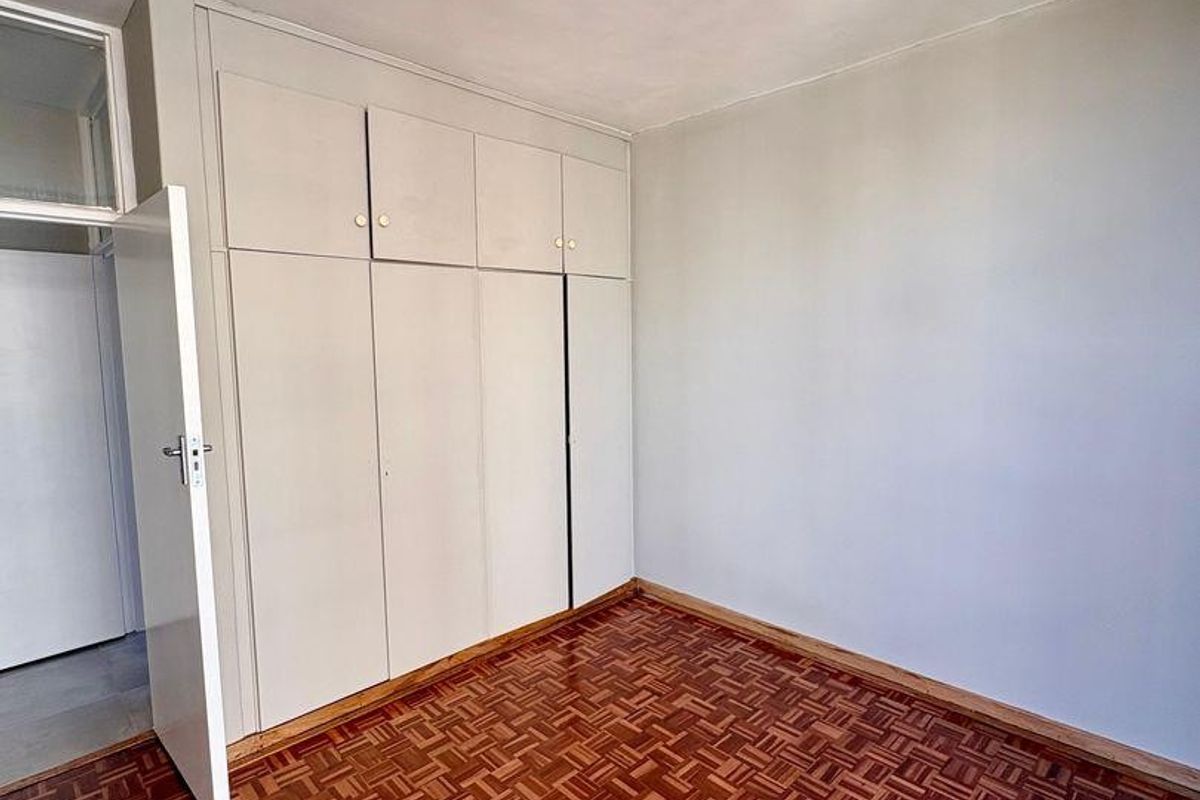 A bright, empty bedroom featuring classic parquet flooring and ample built-in cupboard storage space.