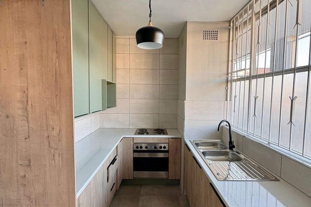 Modern galley-style kitchen featuring light wood-grain cabinetry, stone countertops, integrated stainless steel oven and hob, and a double sink with a matte black faucet.