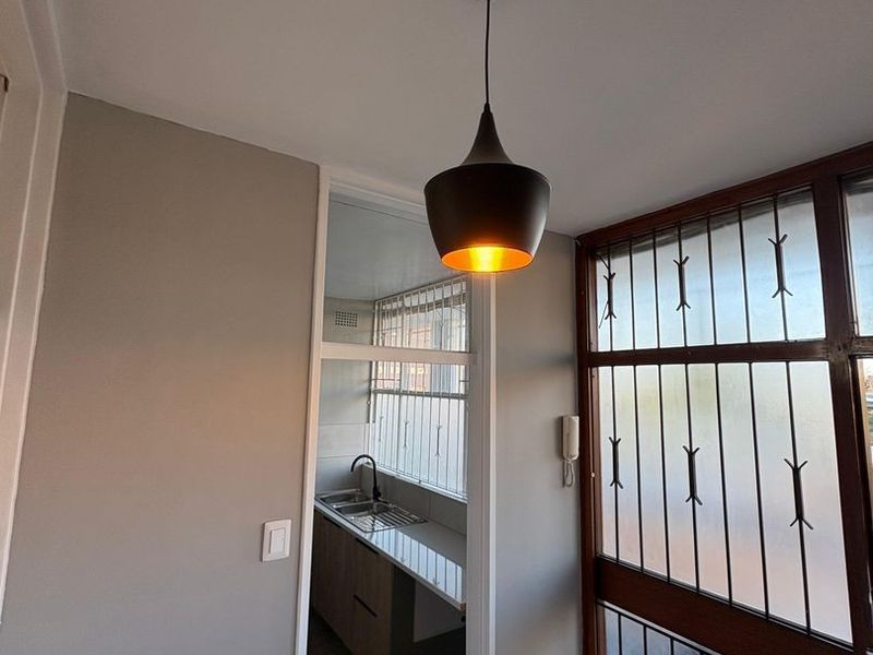 An entrance area featuring tiled flooring, a modern pendant light, and a security gate, with a view into the adjacent kitchen space.