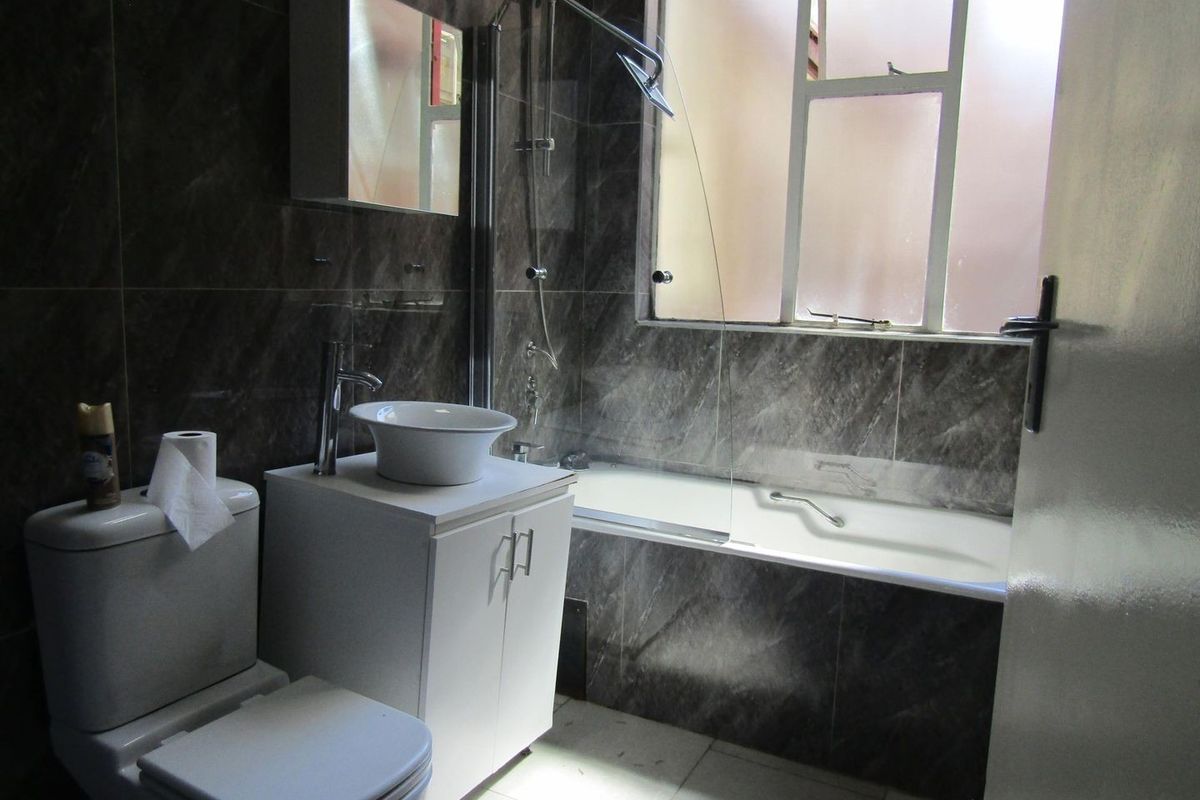 A bathroom featuring dark marble-effect wall tiles, a white vanity with a vessel sink, a toilet, and a bathtub with a shower attachment.