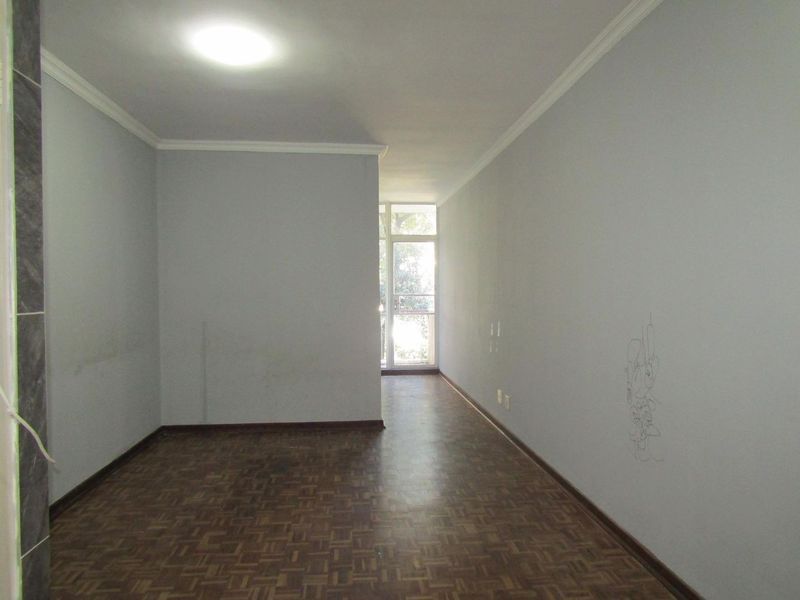 An empty living area featuring parquet flooring, ceiling cornicing, and access to an external balcony through a glass door.