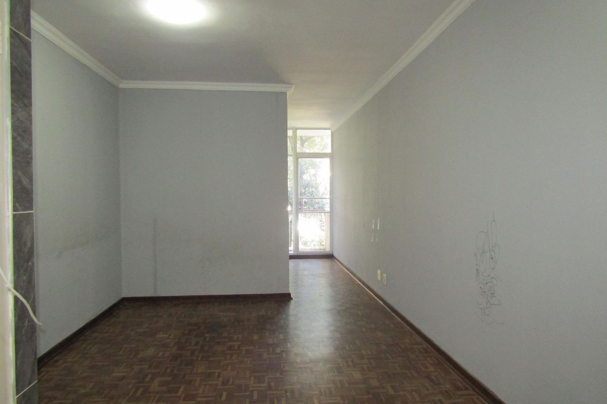 An empty living area featuring parquet flooring, ceiling cornicing, and access to an external balcony through a glass door.