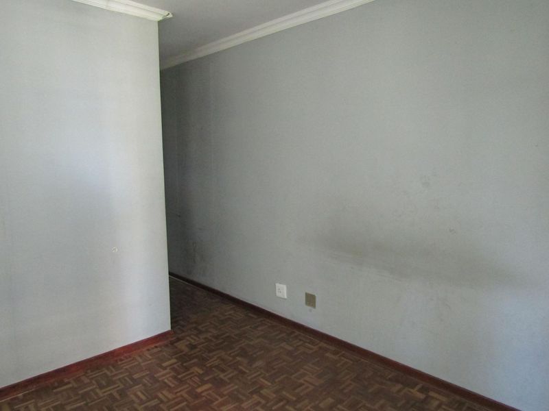 An empty hallway featuring parquet flooring, coving, and neutral walls showing signs of wear and scuffing.