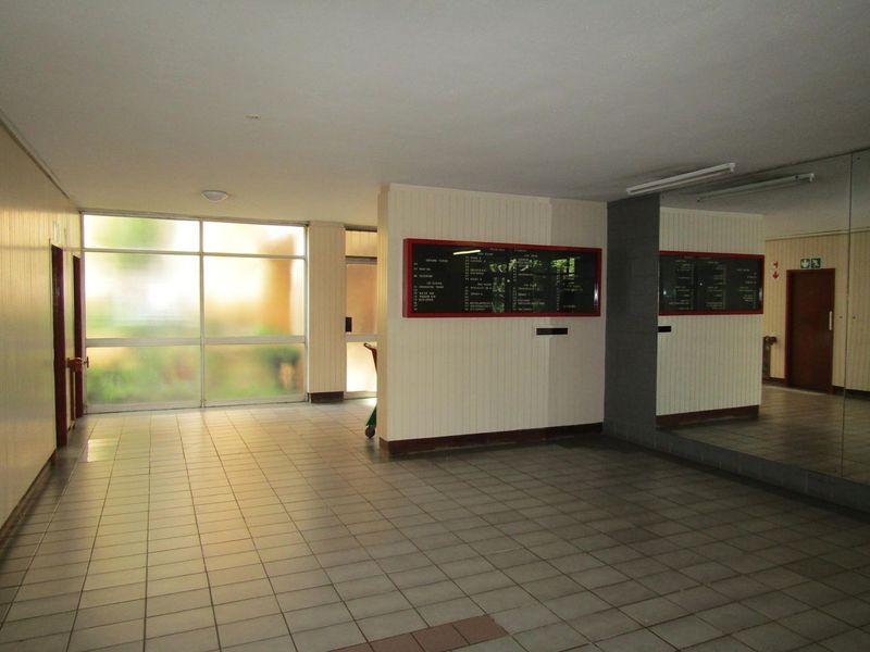 A spacious apartment building entrance lobby featuring tiled flooring, large glass windows, and a wall-mounted directory board.