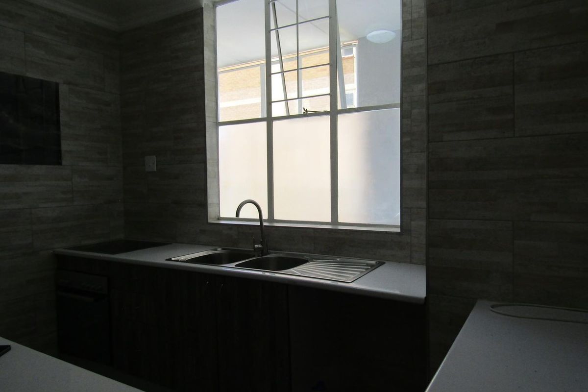 A functional kitchen featuring modern tiled walls, stone countertops, a stainless steel double sink, and built-in oven and hob.