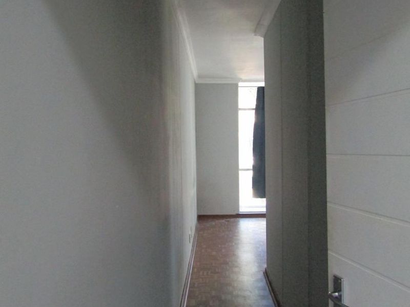 A narrow, empty hallway featuring parquet flooring, white internal doors, and neutral wall finishes, leading towards a naturally lit end space.