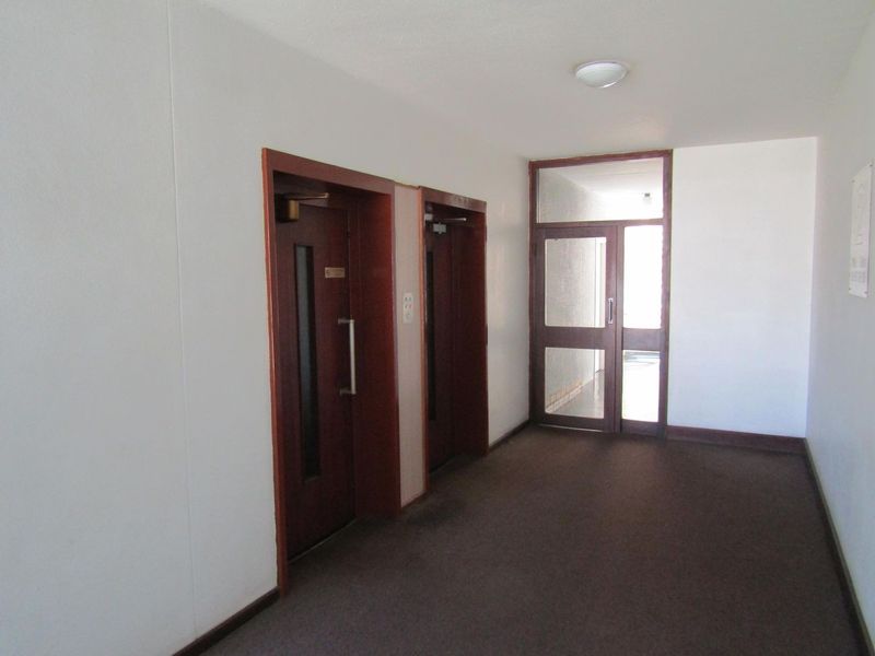 A clean, functional apartment building hallway featuring elevator access and a glass-paneled entry door.