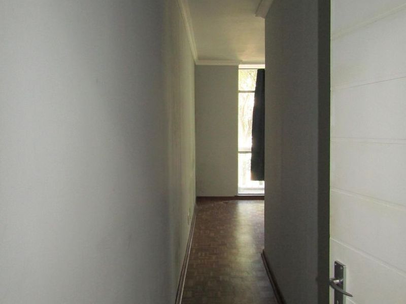 A narrow, empty hallway featuring parquet flooring, coved ceilings, and neutral wall finishes, leading towards a windowed area.