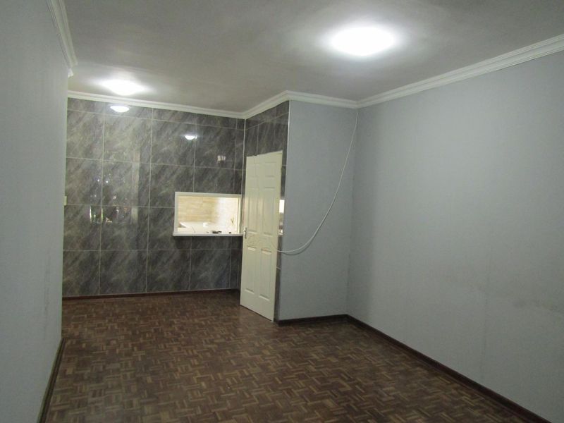 An empty living area featuring parquet flooring, a tiled feature wall with a serving hatch, and coved ceilings.
