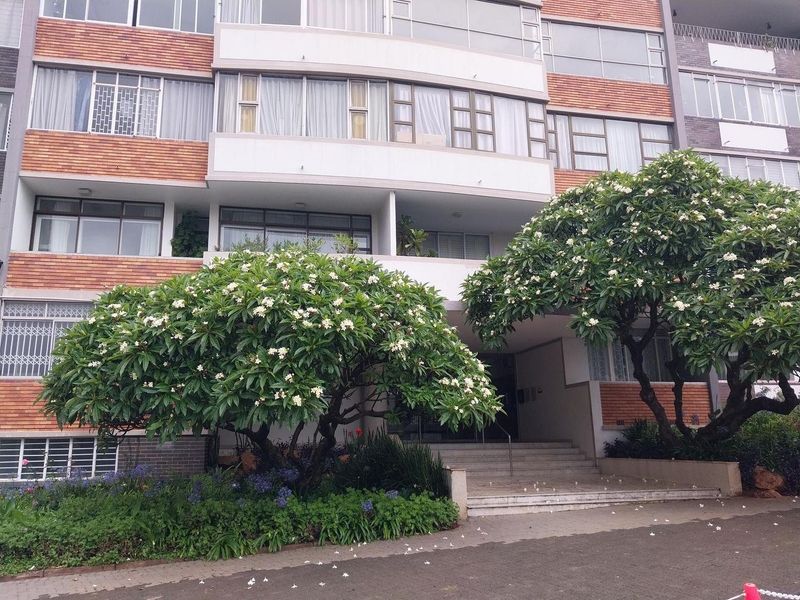 Front elevation of a multi-story apartment building featuring brick detailing, large windows, and a landscaped entrance with concrete stairs.
