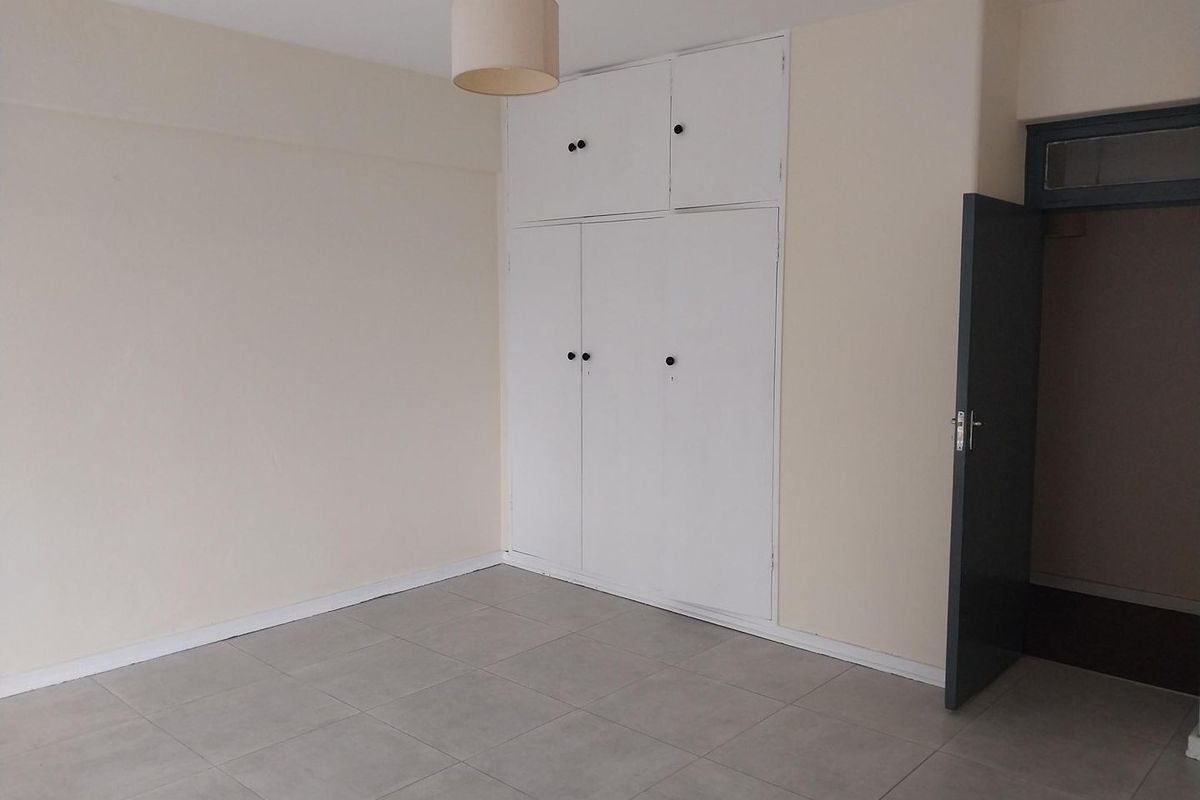 An empty bedroom featuring neutral tiled flooring and white built-in cupboards, providing a clean and versatile space ready for personalization.