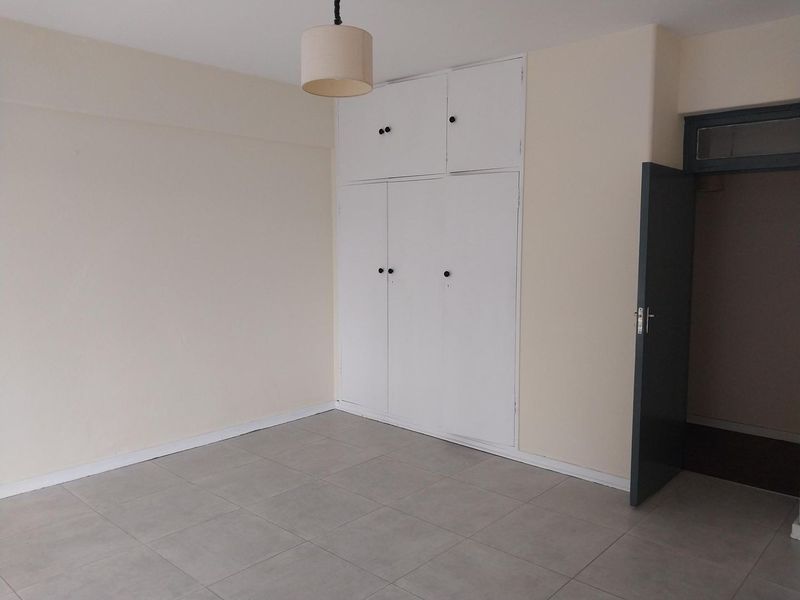 An empty bedroom featuring neutral tiled flooring and white built-in cupboards, providing a clean and versatile space ready for personalization.