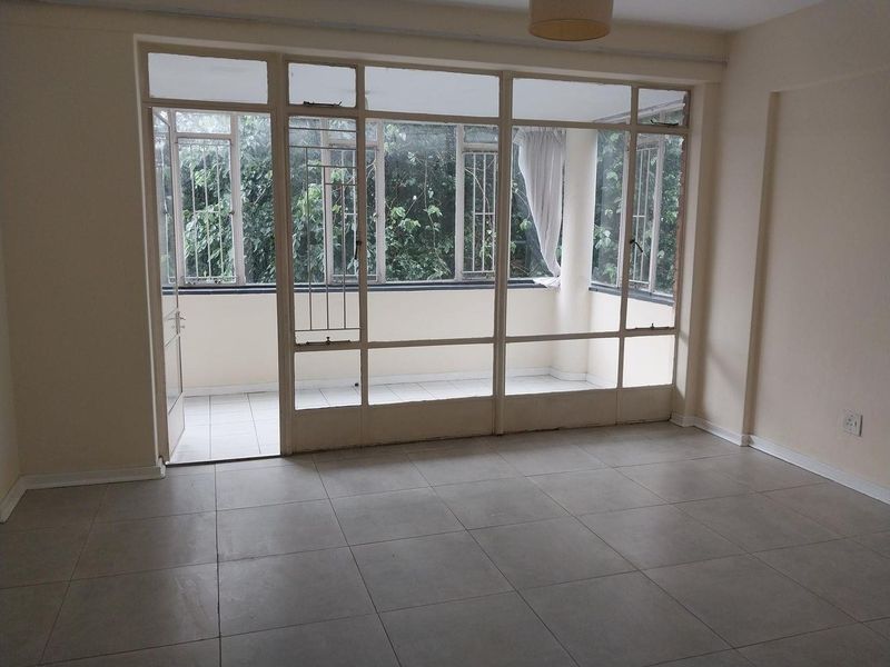 Spacious living area featuring neutral tiled flooring and a large glass partition leading to an enclosed balcony with security bars.