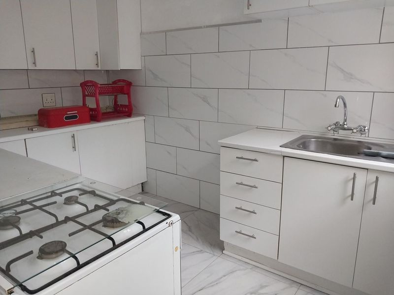 A clean, functional kitchen featuring white cabinetry, marble-look wall and floor tiling, a stainless steel sink, and a built-in gas hob.