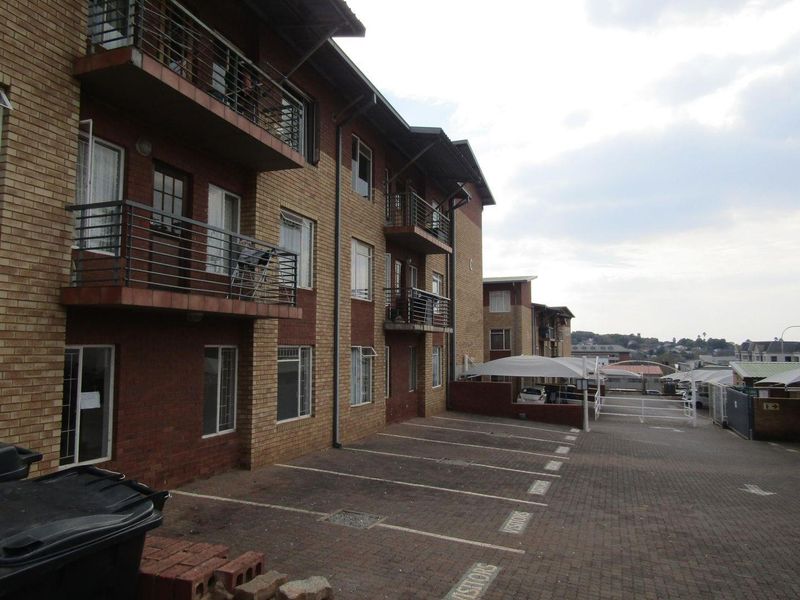 Exterior view of a multi-story apartment complex featuring brick facade, private balconies with metal railings, and a paved visitor parking area.