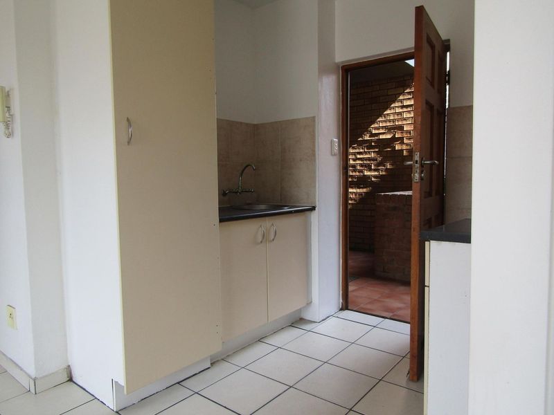 A functional scullery or utility area featuring built-in cabinetry, a sink, and tiled flooring, with direct access to an outdoor space.