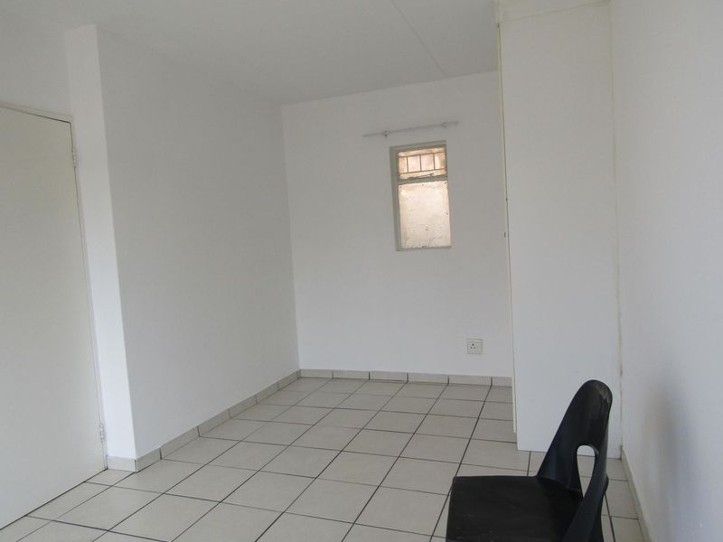 A vacant bedroom featuring neutral tiled flooring and a built-in cupboard, offering a clean and simple space ready for personalization.