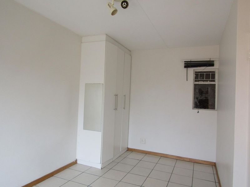 An empty bedroom featuring tiled flooring, a built-in wardrobe, and a window with a damaged pane.