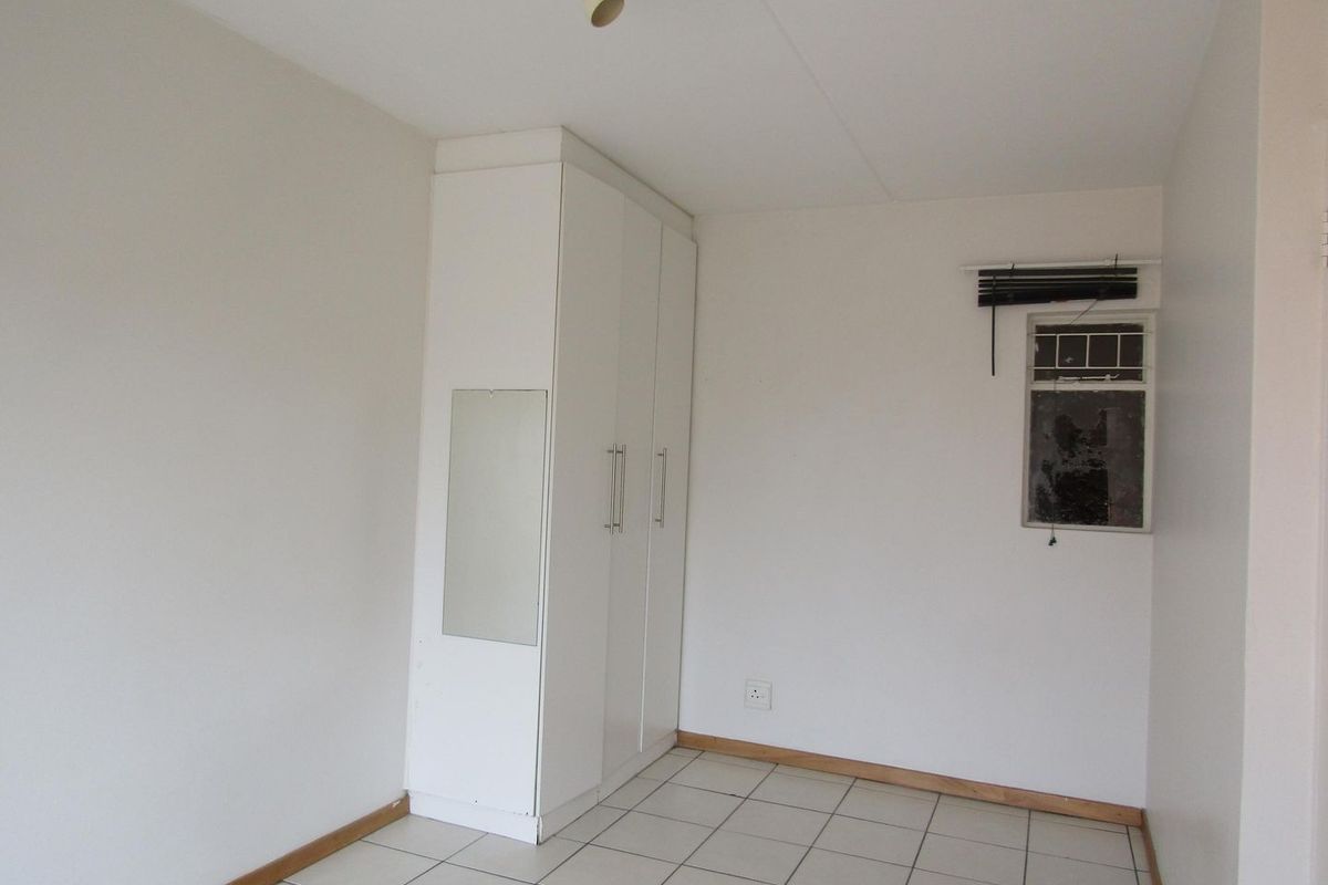 An empty bedroom featuring tiled flooring, a built-in wardrobe, and a window with a damaged pane.