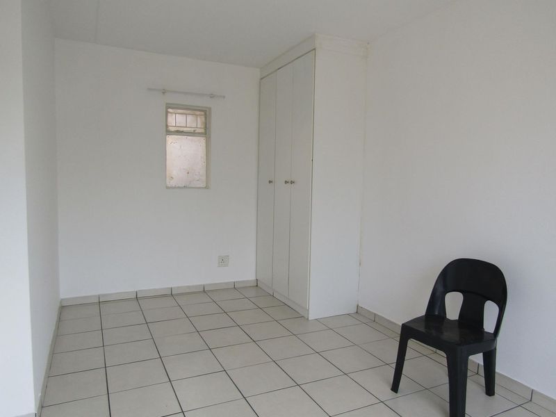 A simple, vacant bedroom featuring neutral tiled flooring and a built-in wardrobe, offering a blank canvas for personalization.