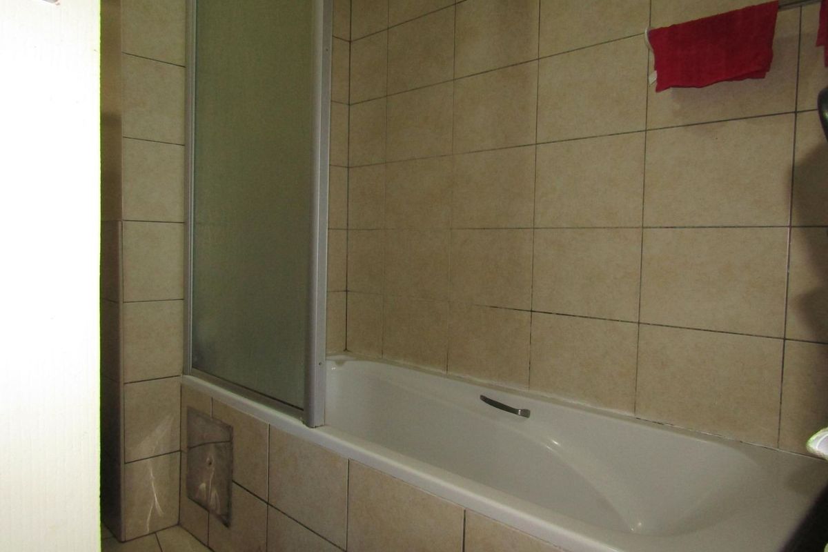 A functional bathroom featuring a bathtub with a glass shower screen and neutral wall tiling.