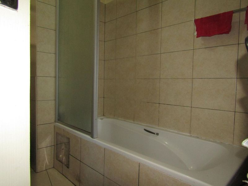 A functional bathroom featuring a bathtub with a glass shower screen and neutral wall tiling.