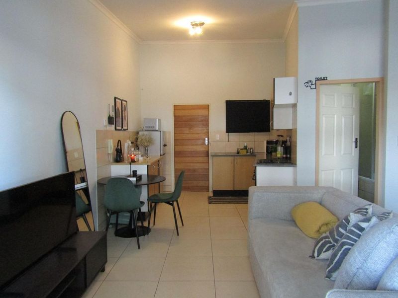 Open-plan living area featuring tiled floors, a compact kitchen with built-in cabinetry, and direct access to a separate bathroom.