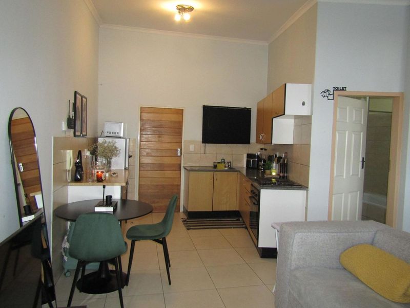 Open-plan kitchen and living area featuring tiled flooring, built-in cabinetry with integrated oven and hob, and direct access to an adjacent bathroom.