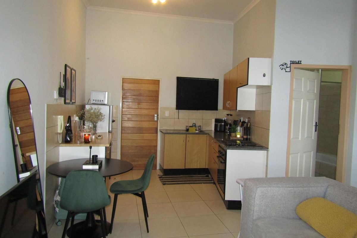 Open-plan kitchen and living area featuring tiled flooring, built-in cabinetry with integrated oven and hob, and direct access to an adjacent bathroom.