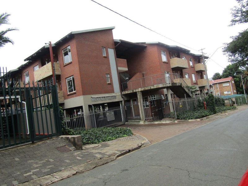 Exterior view of Melville Mews apartment complex featuring face brick architecture, secure perimeter fencing, and paved access.