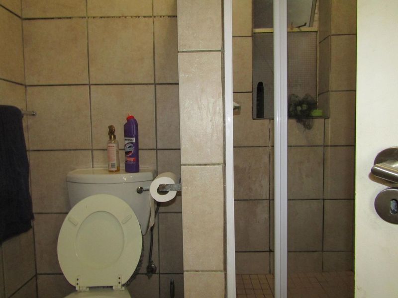 A compact bathroom featuring a toilet and a shower enclosure with tiled walls and flooring, showing signs of wear and dated finishes.