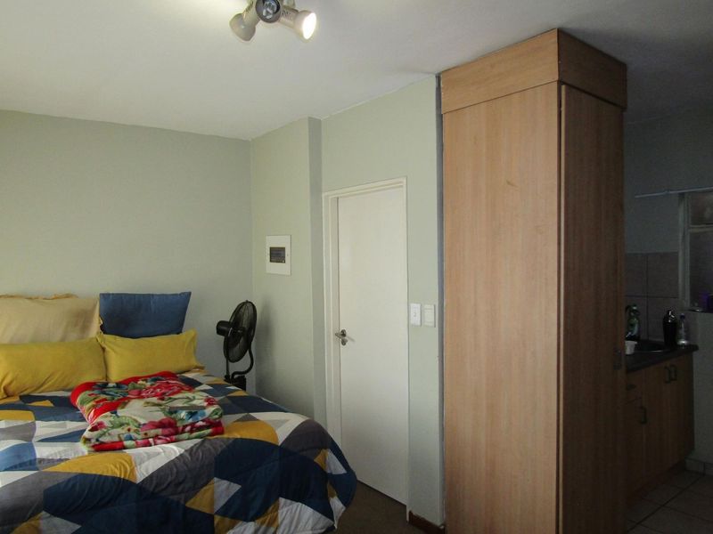 An open-plan studio apartment featuring a bedroom area with built-in wardrobe and a compact kitchen corner with cabinetry and sink.
