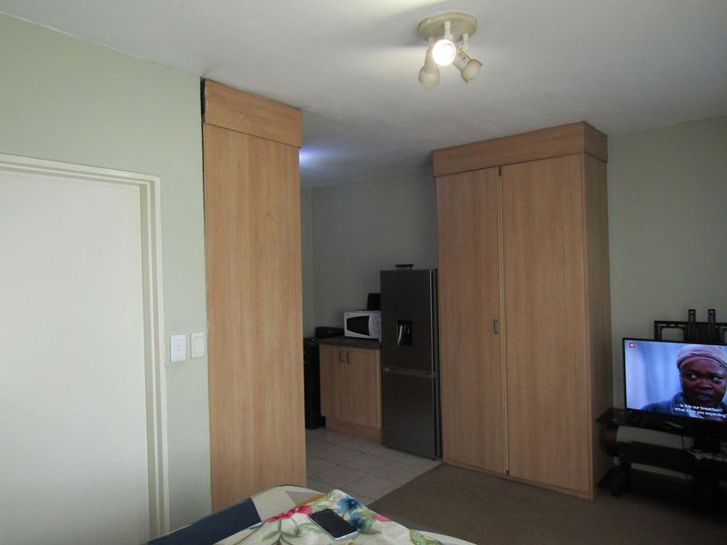 Open plan living area featuring built-in cupboards and a compact kitchen corner with tiled flooring.