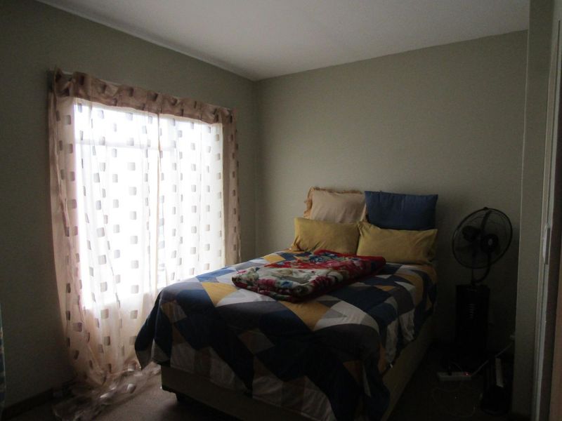 A standard bedroom featuring neutral wall tones and a window with patterned curtains, providing natural light to the space.