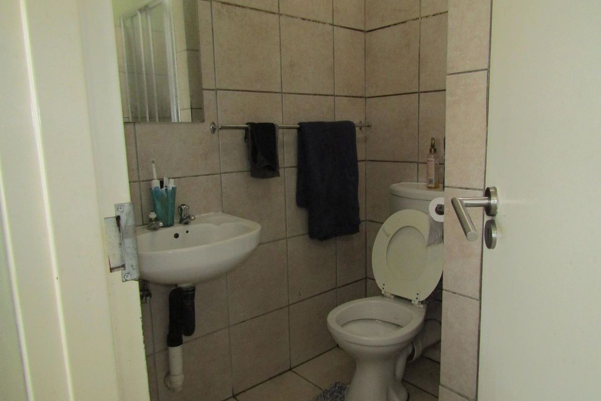 A compact bathroom featuring ceramic wall and floor tiles, a wall-mounted basin, and a standard toilet.