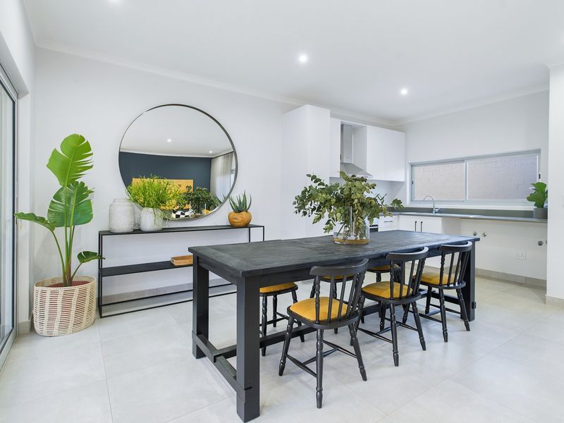 A bright open-plan living and kitchen area featuring modern white cabinetry, recessed lighting, tiled floors, and large sliding glass doors leading outdoors.