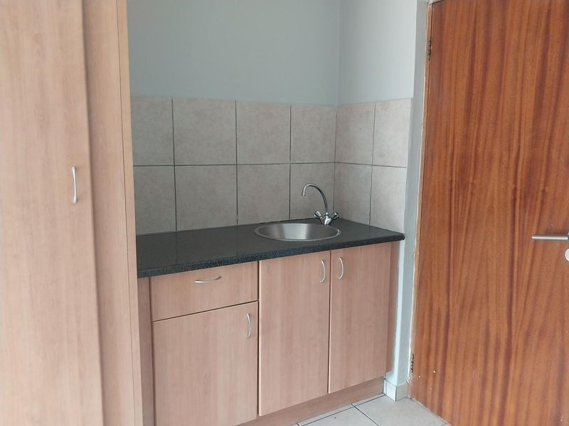 A compact scullery or kitchenette area featuring laminate cabinetry, a stainless steel sink, and neutral ceramic wall tiling.
