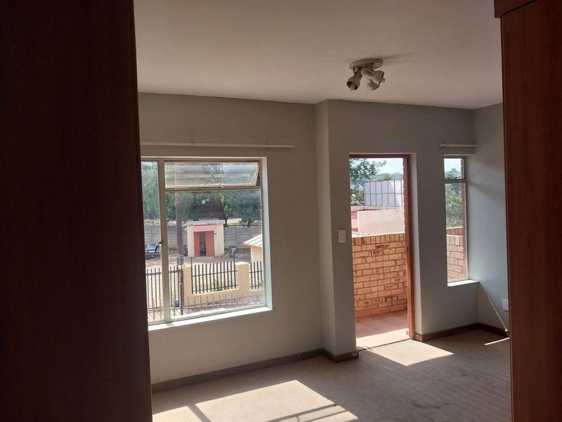 An empty bedroom featuring carpet flooring, aluminium window frames, and direct access to an outdoor balcony area.