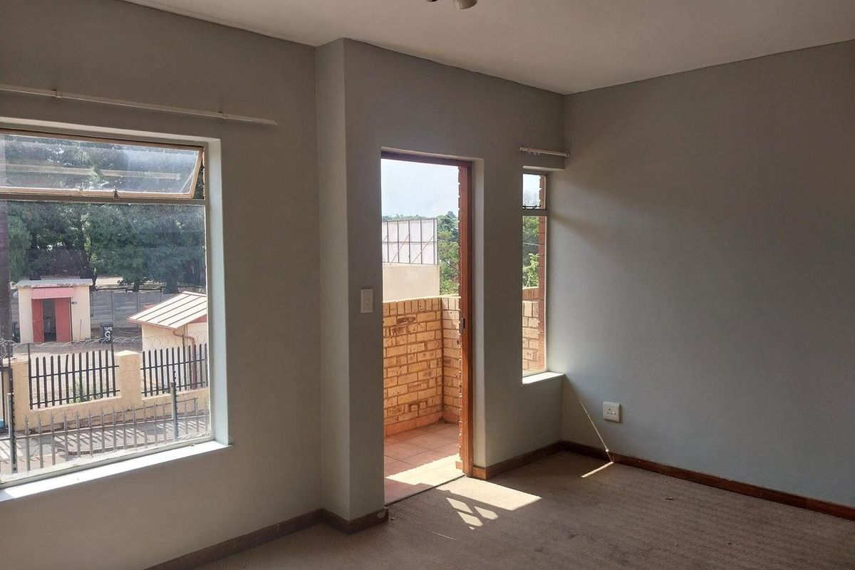An empty living room featuring carpet flooring, neutral walls, and direct access to a small balcony through a doorway.