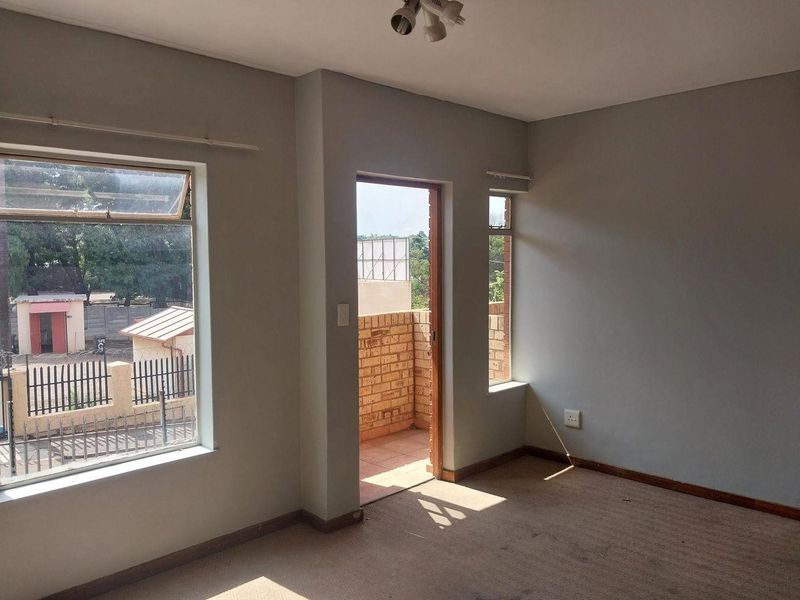 An empty living room featuring carpet flooring, neutral walls, and direct access to a small balcony through a doorway.