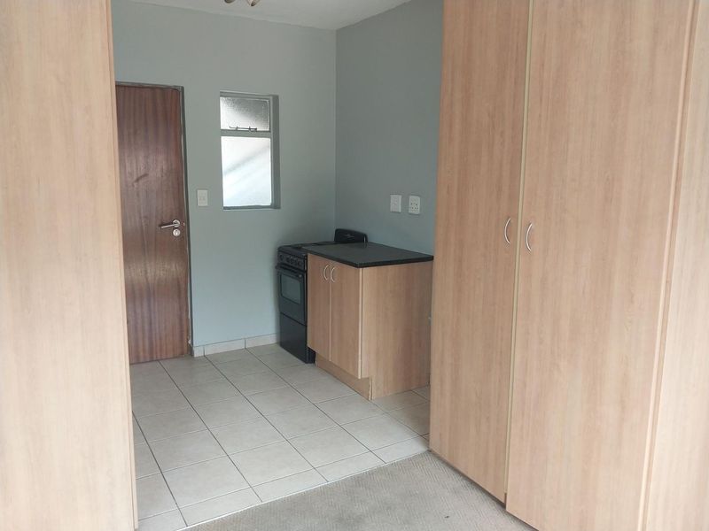 A compact kitchen area featuring built-in cabinetry, a freestanding stove, and tiled flooring, adjacent to a bedroom space with built-in wardrobes.