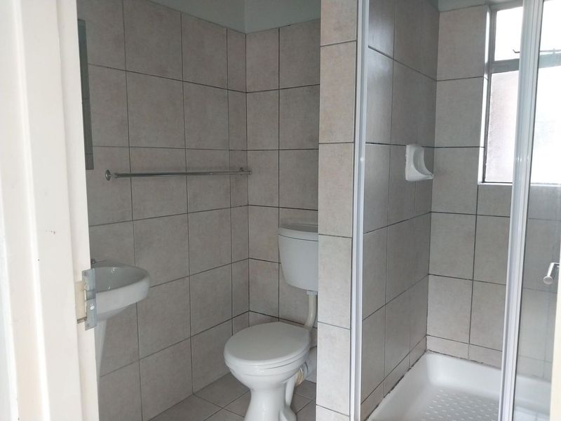 A functional bathroom featuring a pedestal basin, toilet, and a separate shower enclosure with neutral wall and floor tiling.